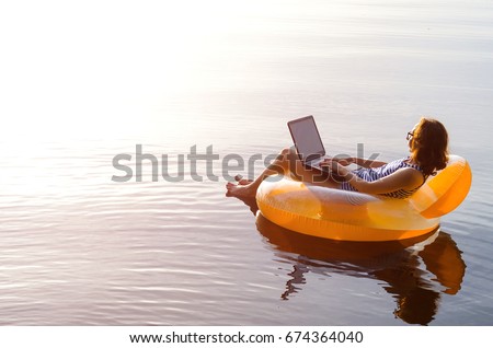 Business woman working on a laptop in an inflatable ring in the water, a copy of the free space. Workaholic, work on vacation. Royalty-Free Stock Photo #674364040