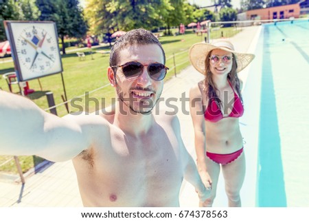 Young loving couple beside the pool takes a selfie in swimsuit. Concept of young people having fun in summertime
