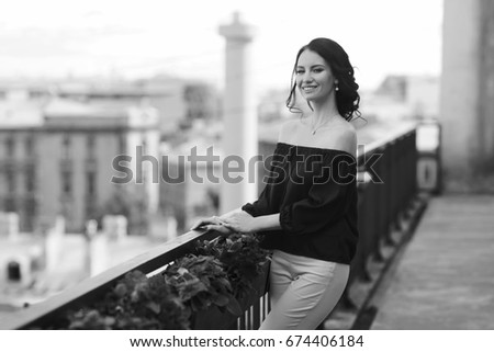 Young beautiful caucasian brunette woman with hairstyle posing at summer terrace with with on city buildings. Attractive girl in trousers and red blouse.