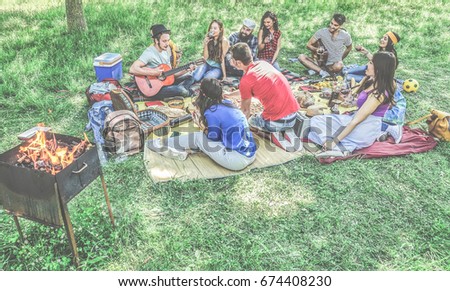Group of friends making picnic barbecue outdoor in city park - Young people having fun playing music and relaxing at bbq party sitting on grass - Main focus on bottom guys - Contrast filter