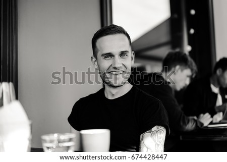 Handsome tattooed man on a summer terrace in a city cafe is drinking wine. Street Cafe.