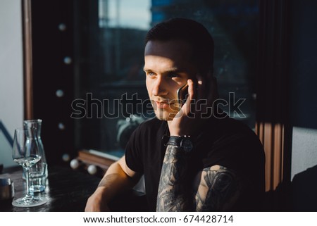 Handsome tattooed young man talking on the phone, close-up portrait, outdoors
