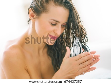 Happy young woman applying hair conditioner in bathtub Royalty-Free Stock Photo #674437357