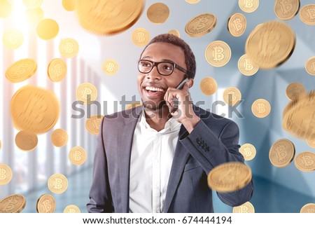 Portrait of an African American businessman wearing glasses and talking on a smartphone and standing in an office under a bitcoin rain.