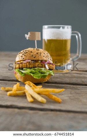 Close up fries with burger and beer glass on table against wall