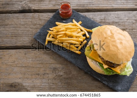 High angle view of cheeseburger with french fries and sauce on slate at table