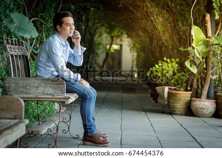 Middle aged Asian men sit on a wooden bench in the garden. And are playing mobile phones.