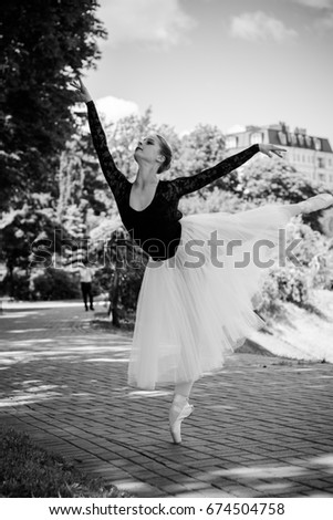 Ballet dancer in white tutu posing in city near garden. Town background and dynamic training body 