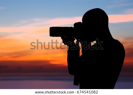Photographer taking pictures, silhouette of a man with camera over beautiful orange sunset background, photographing amazing view of a nature near the beach