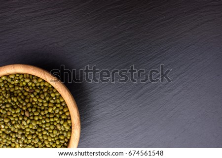 mung bean in a wooden cup on a black stone board background, space for text, beans.