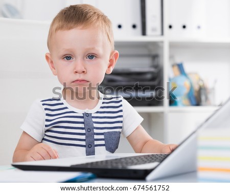 Cute child is surfing in internet on laptop in the office.