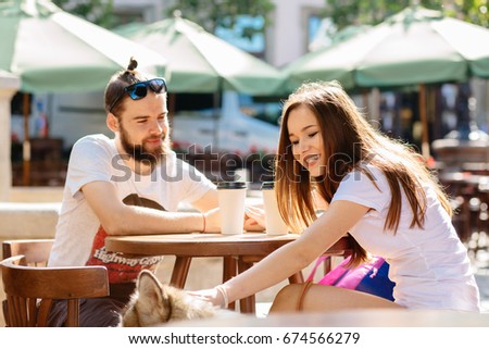 Family, pet, animal and people concept - Cheerful friendly picture of lovely hipster couple with their dog drinking coffee while sitting on the street cafe in summer, outdoor