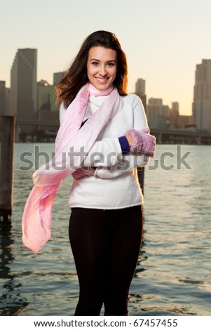 Pretty young woman lifestyle with winter clothing along a seawall on the bay with a downtown skyline at sunset.