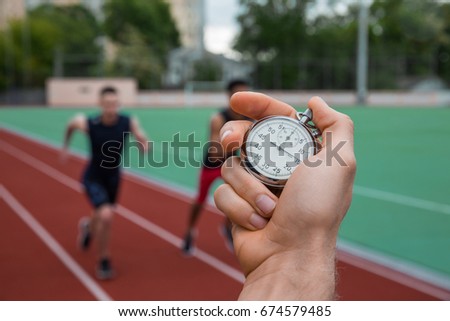 Picture of young athlete men run on running track outdoors. Historic stop watch time measurement.