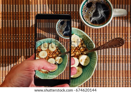 Male person making picture of healthy breakfast of muesli cereals with banana and fresh coffee
