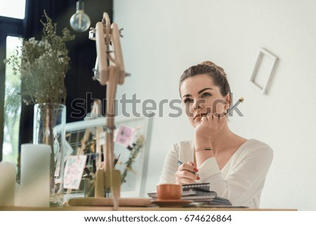 pensive attractive female florist holding dry flower and sitting in creative office