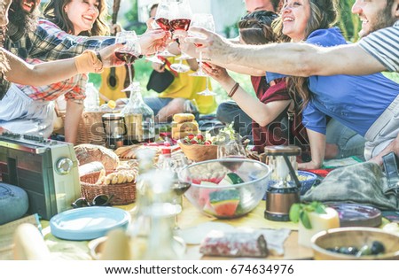 Happy friends cheering with wine glasses at pic-nic lunch outdoor - Young students having fun doing a toast and eating on nature - Food and youth concept - Focus on center glasses - Vintage filter