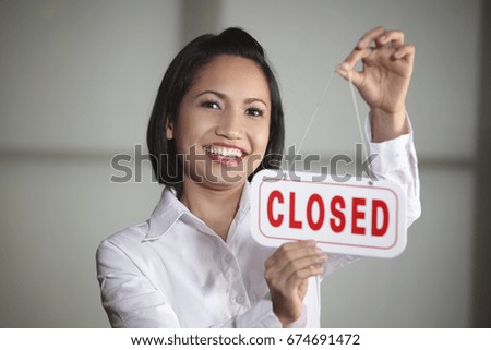 Young woman hanging Closed sign on door, smiling