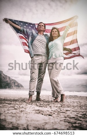 Full length of couple holding American flag against sky at beach 