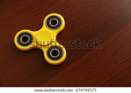 Fidget Spinner on a wooden table is useless machine designed to spin but became a popular toy for people who wanted to cut boredom and stress.