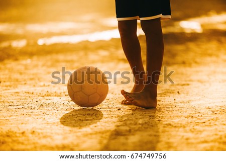 An action and motion picture of an old ball and foot of a kid who is playing football in the sunshine day for exercise.Low key style.