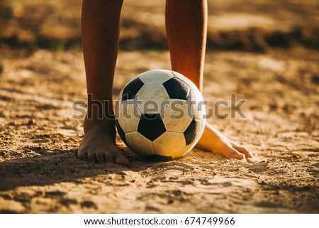 An action and motion picture of an old ball and foot of a kid who is playing football in the sunshine day for exercise.Low key style.
