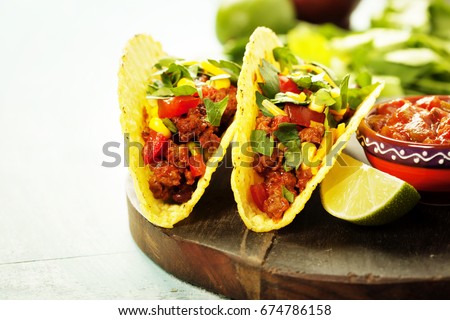 Mexican nachos chips and tacos with meat, beans and salsa on rustic background