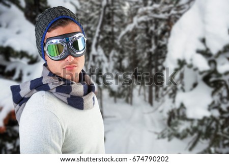 Man wearing aviator goggles against white background against snow covered pine trees on alp mountain slope