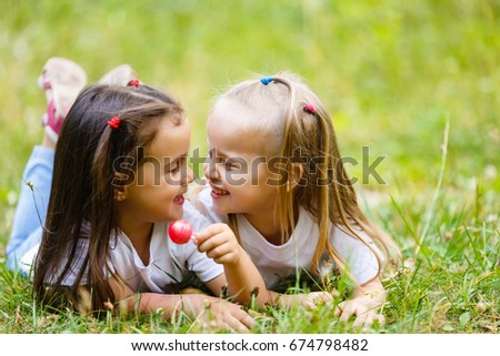 Two little girls relaxing and eating a lollipop at a park