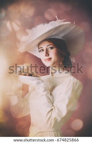 photo of beautiful young woman in vintage dress with plate full of chocolates. Photo im old color image style with bokeh