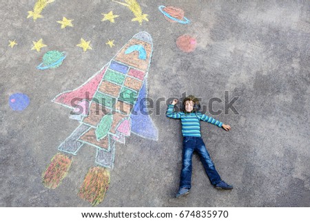Funny little kid boy flying in universe by a space shuttle picture painting with colorful chalks. Creative leisure for children outdoors in summer.