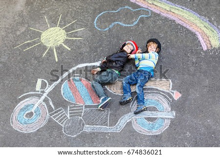 Creative leisure for children: two little funny friends in helmet having fun with motorcycle picture drawing with colorful chalks. Children, lifestyle, fun concept.
