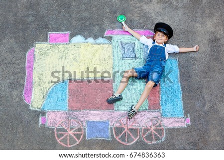 Happy little kid boy having fun with train or steam locomotive picture drawing with colorful chalks on ground. Children, lifestyle, fun concept. funny child playing 
