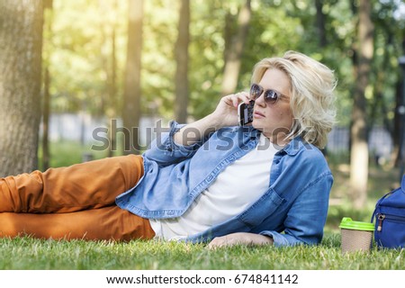 Funny girl using a cellphone on a grass park with a green background. Communication anywhere in the world