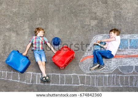 Two little kids boys having fun with train picture drawing with colorful chalks on ground. Children having fun with chalk and crayon painting and game going on vacations. Friends with suitcases.