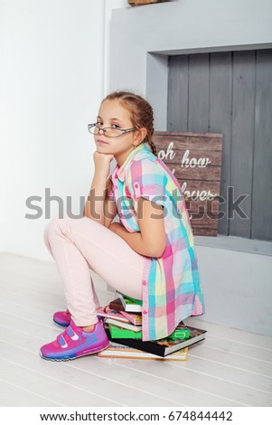 The child is sitting on books in glasses. The concept of education and childhood.