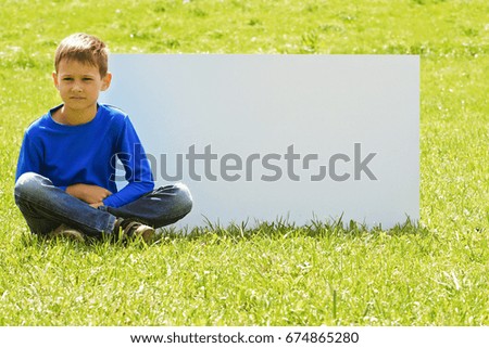 Child sitting on the grass against blank white placard board