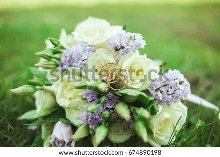 Beautiful bridal bouquet of bride on green grass with gold rings.