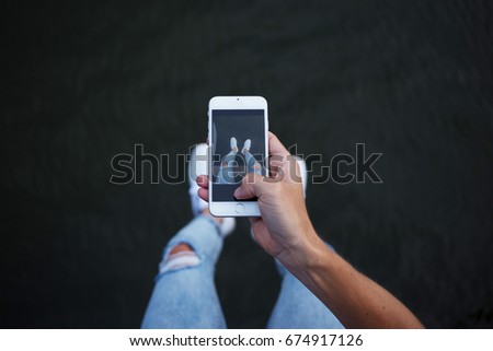 POV of man in trendy fashionable hipster skinny denim jeans making photos of his legs and feet in white sneakers on smartphone for social media