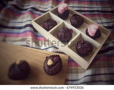Closeup chocolate cupcake in wooden box at the right side of colorful pattern print table cloth,blurred cupcake out of box at the left side,vintage design,warm light tone,blurry light background