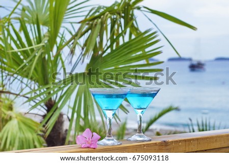 Two martinis on a summer terrace with palm trees and a beach