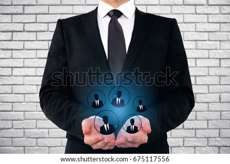 Businessman holding glowing HR hologram on brick wall background. Hiring concept 