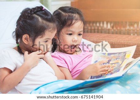 Lovely twin sister two child girls having fun to read a cartoon book together in their room