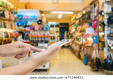 Man use mobile phone, blur image of women's bag shop as background.