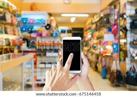Man use mobile phone, blur image of women's bag shop as background.