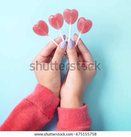 Holding Valentine's heart shape lollipop candy on sky blue background