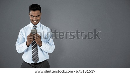 Smiling businessman using mobile phone against grey background
