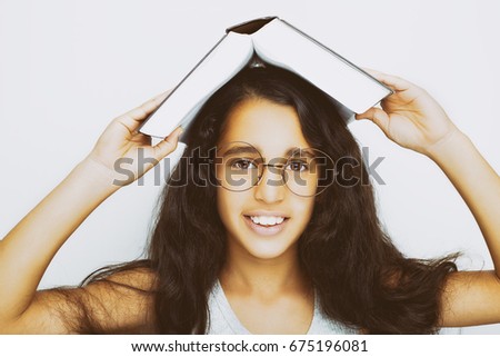 Adorable girl studying with eyeglasses and book on the head on white background