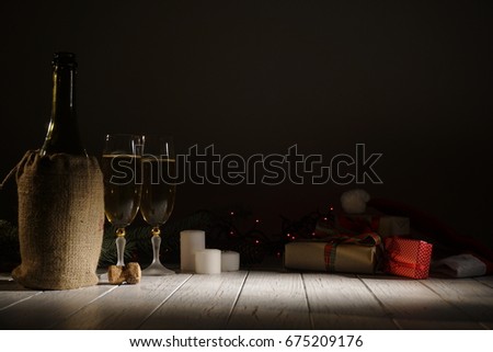 Winter composition consisting of bottle of wine, glasses of champagne, candles, gifts and galrands in the dark room.
