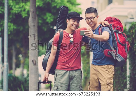 Joyful Vietnamese friends with toothy smiles posing for selfie while taking walk in city center, blurred background